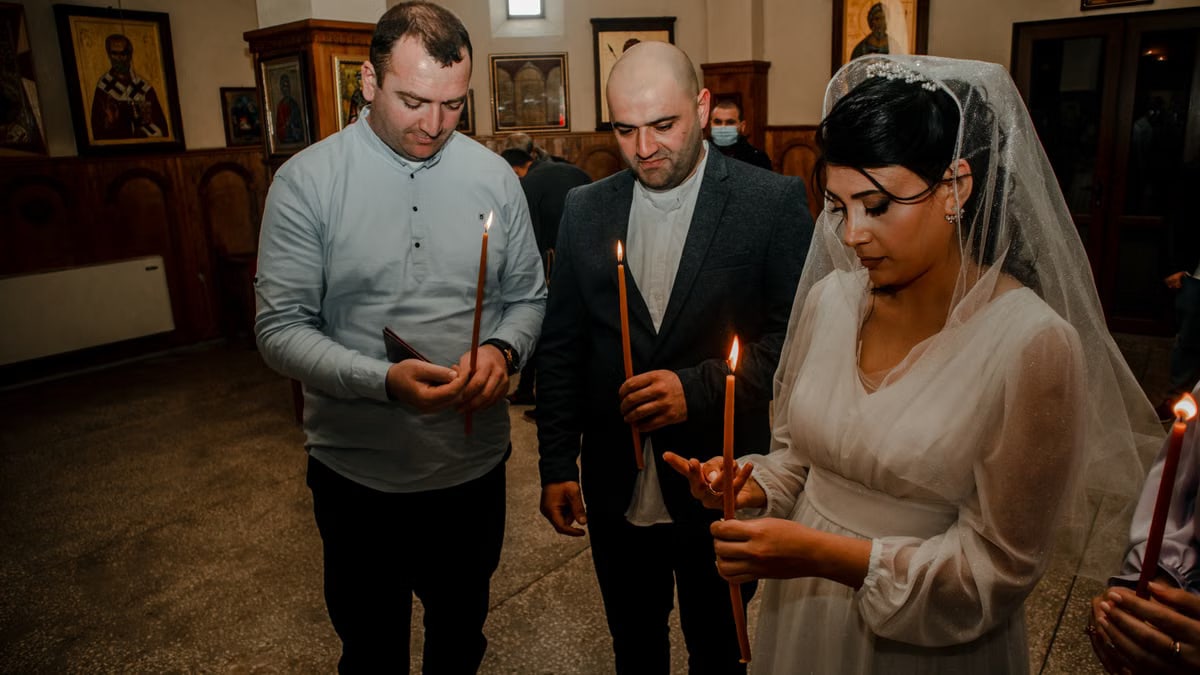 Bride and guests holding candles during an Orthodox wedding ceremony in a church setting.