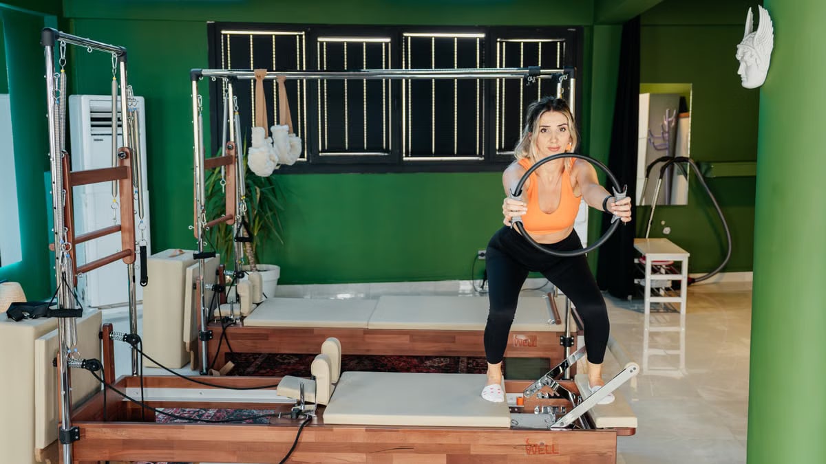 Fitness enthusiast practicing Pilates on a reformer machine in a modern, brightly lit studio.