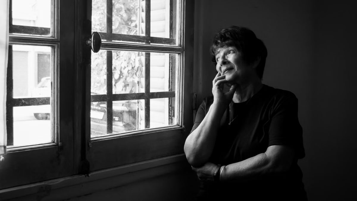 Black and white portrait of a thoughtful elderly woman gazing out a window.